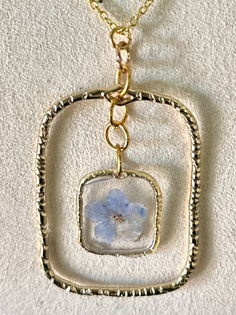 Gold-framed botanical necklace with five-petal blue flower
