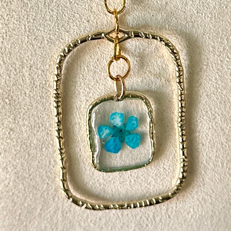 Gold-framed botanical necklace with bright blue flower