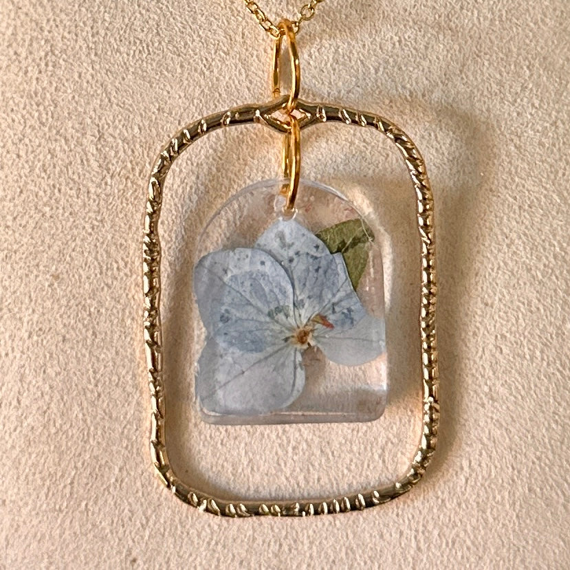Gold-framed botanical necklace with blue flower