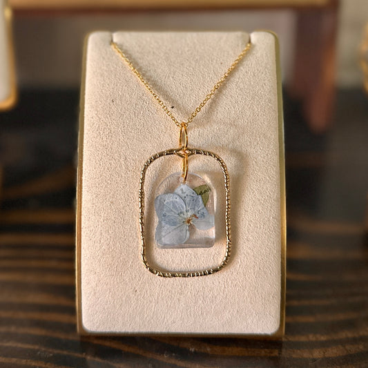 Gold-framed botanical necklace with blue flower