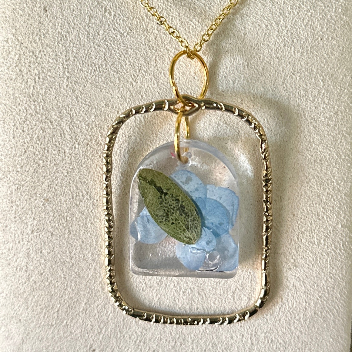 Gold-framed botanical necklace with blue flower