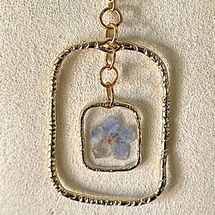 Gold-framed botanical necklace with five-petal blue flower
