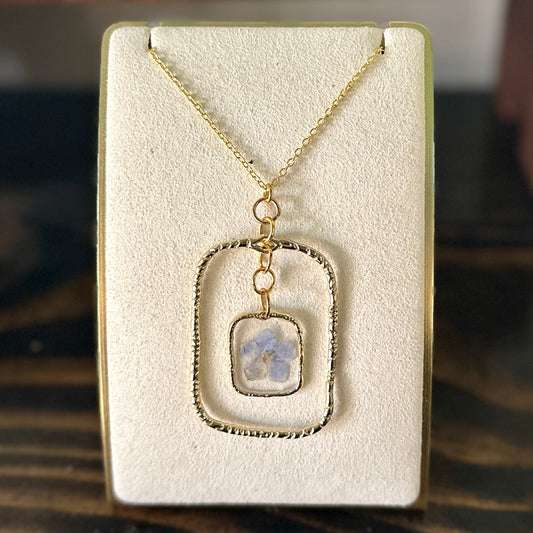 Gold-framed botanical necklace with five-petal blue flower