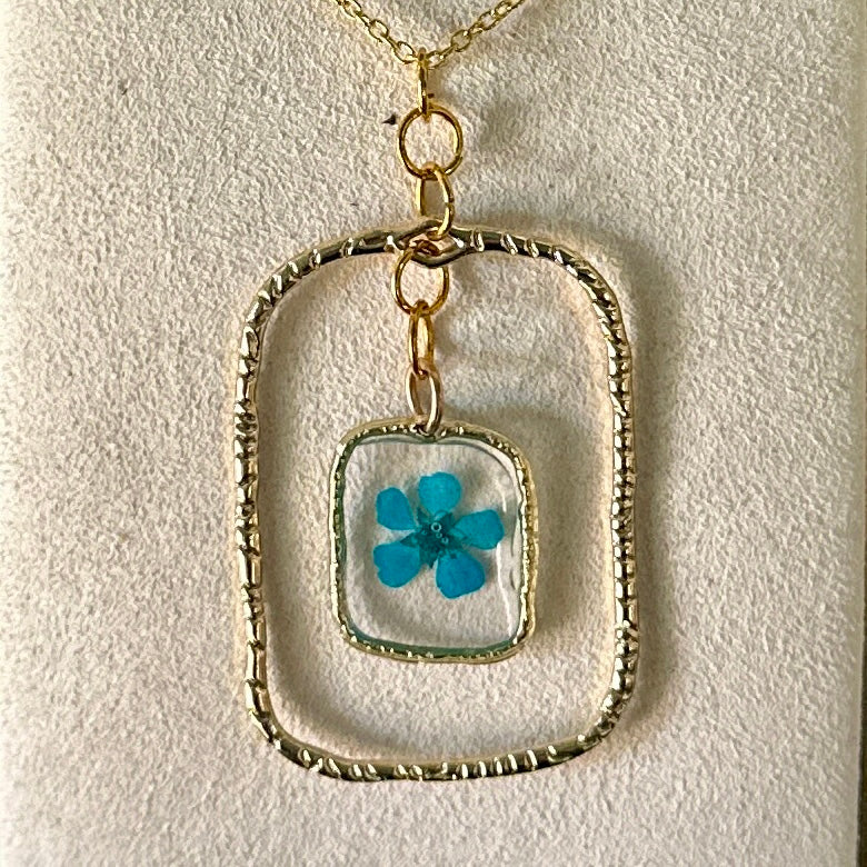 Gold-framed botanical necklace with bright blue flower