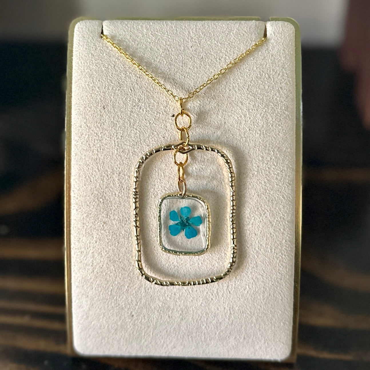 Gold-framed botanical necklace with bright blue flower