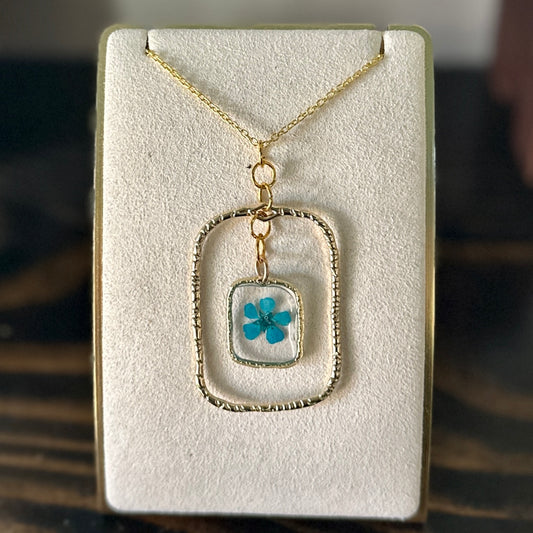 Gold-framed botanical necklace with bright blue flower