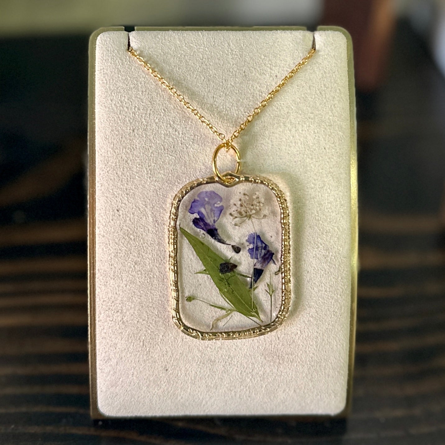 Gold-framed botanical necklace (violet, green, and white)