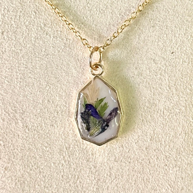 Gold-framed necklace with violet and green botanicals in white resin