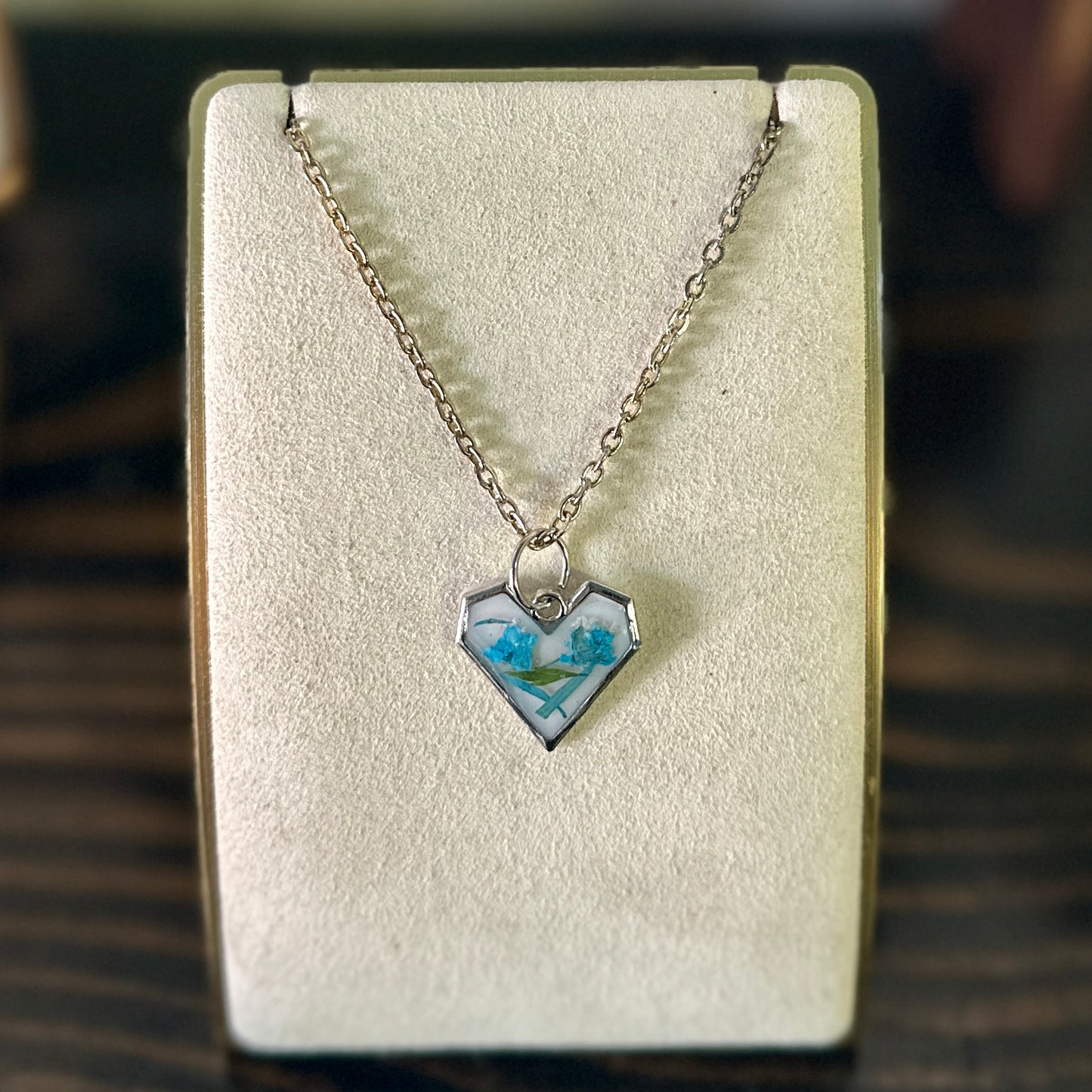 Silver-framed heart necklace with blue and green botanicals in white resin