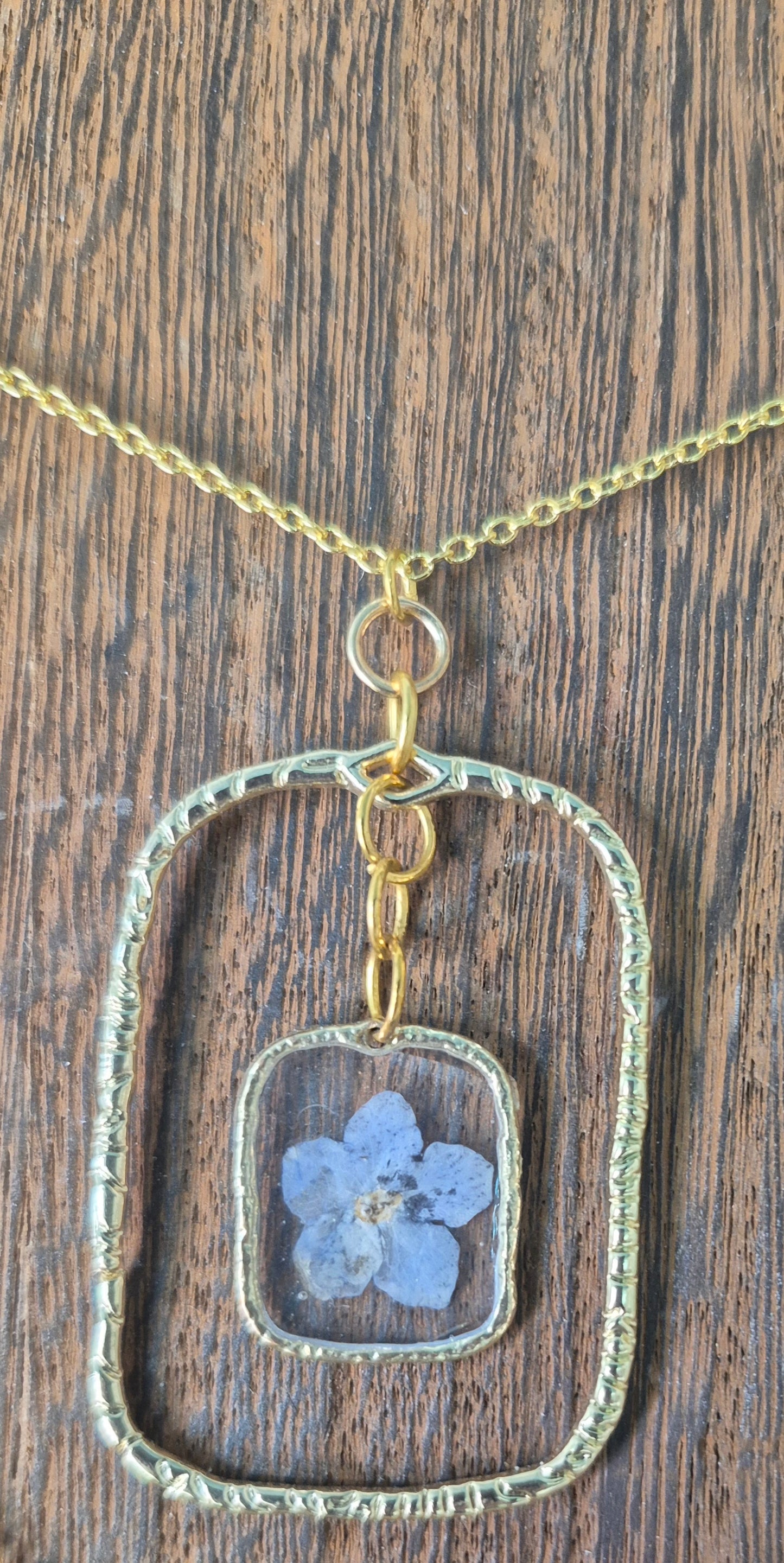 Gold-framed botanical necklace with five-petal blue flower